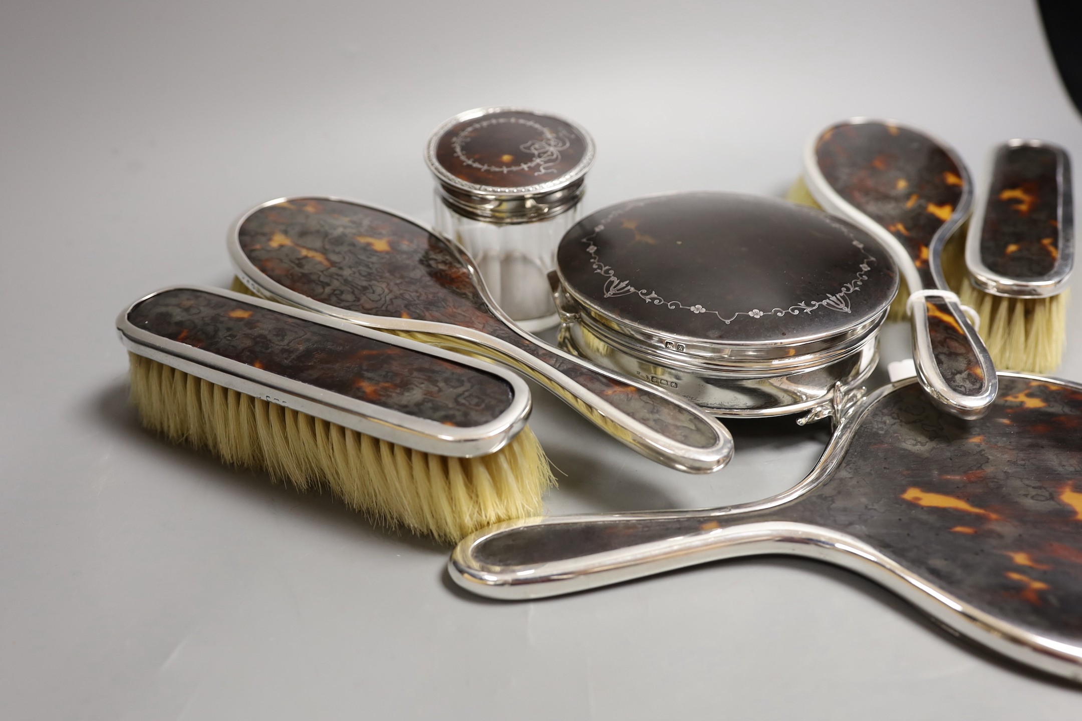 A matched George V seven piece silver and tortoiseshell pique mounted mirror, brush, toilet jar and trinket box set, marks rubbed, trinket box Birmingham, 1925, 12.4cm.